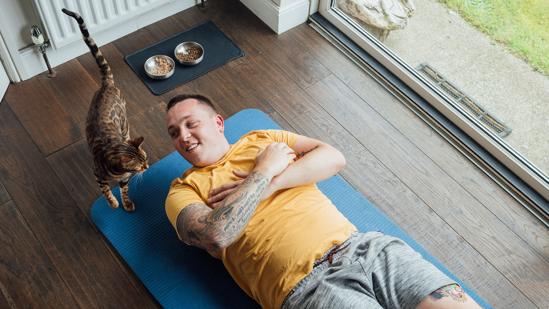 Man hemmatränar på en yogamatta tillsammans med sin katt